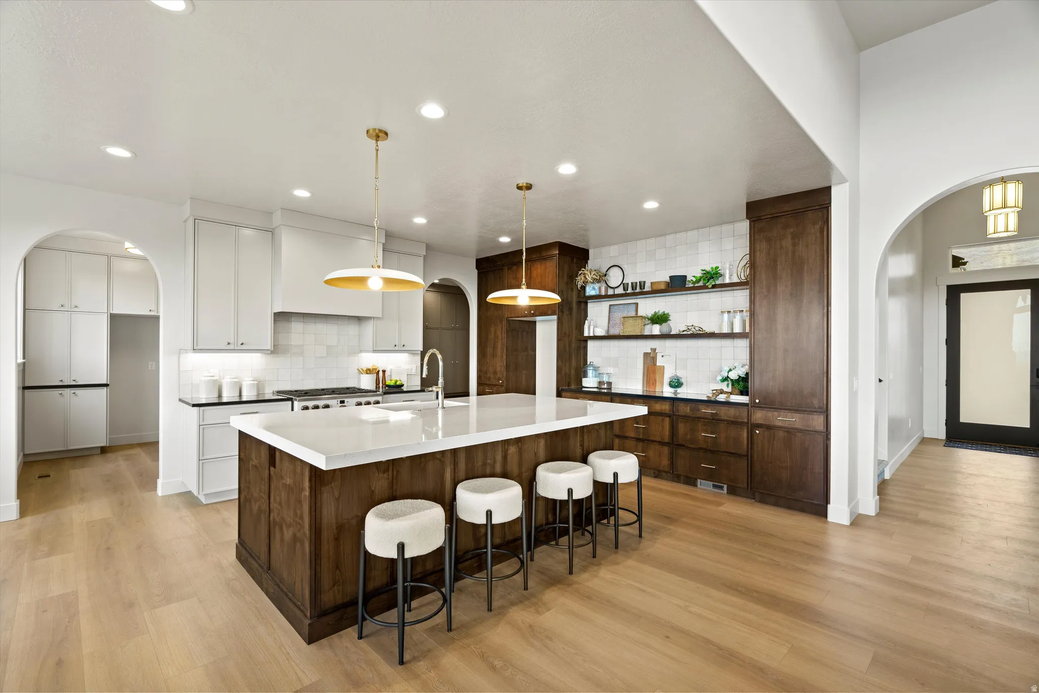 Two tone kitchen with arched walkways, two tone cabinetry, a kitchen bar, light wood-style flooring, and a large island