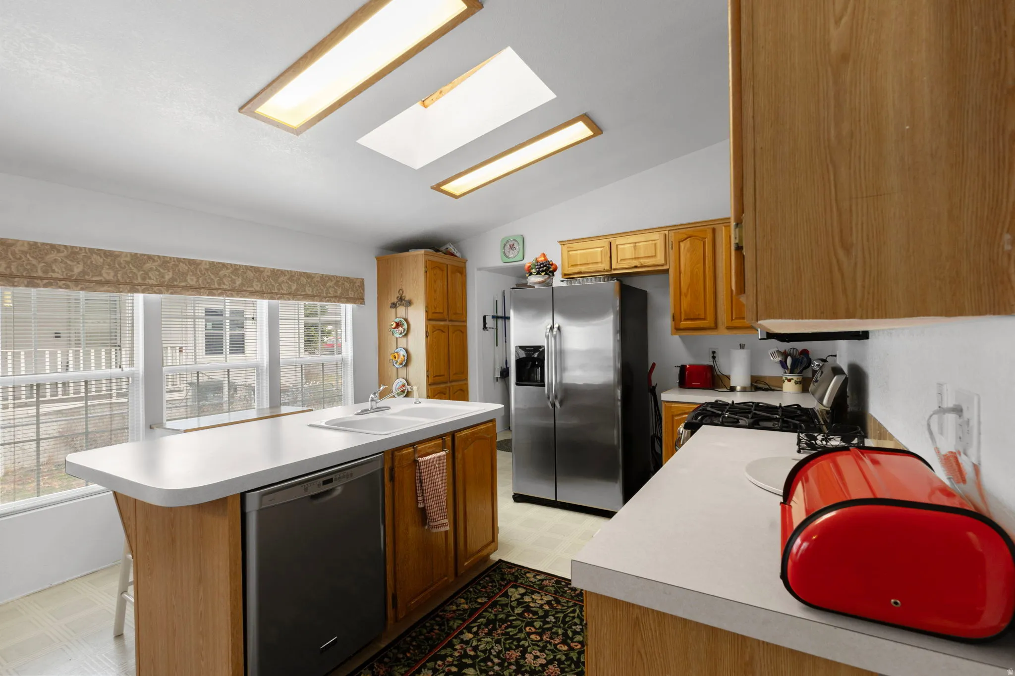 Kitchen with a skylight, light flooring, stainless steel appliances, vaulted ceiling, and light countertops