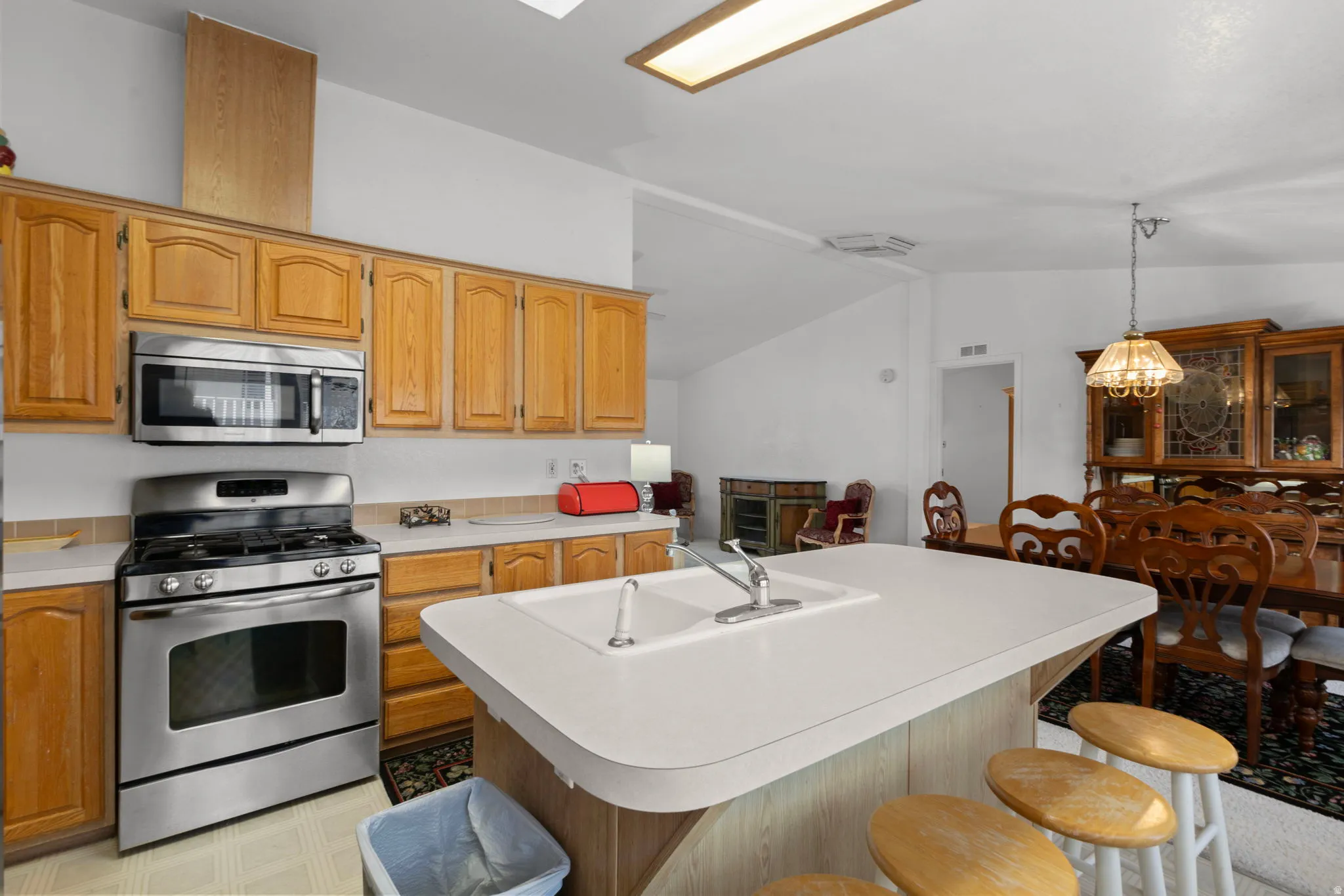 Kitchen featuring a kitchen bar, stainless steel appliances, light countertops, a kitchen island with sink, and lofted ceiling