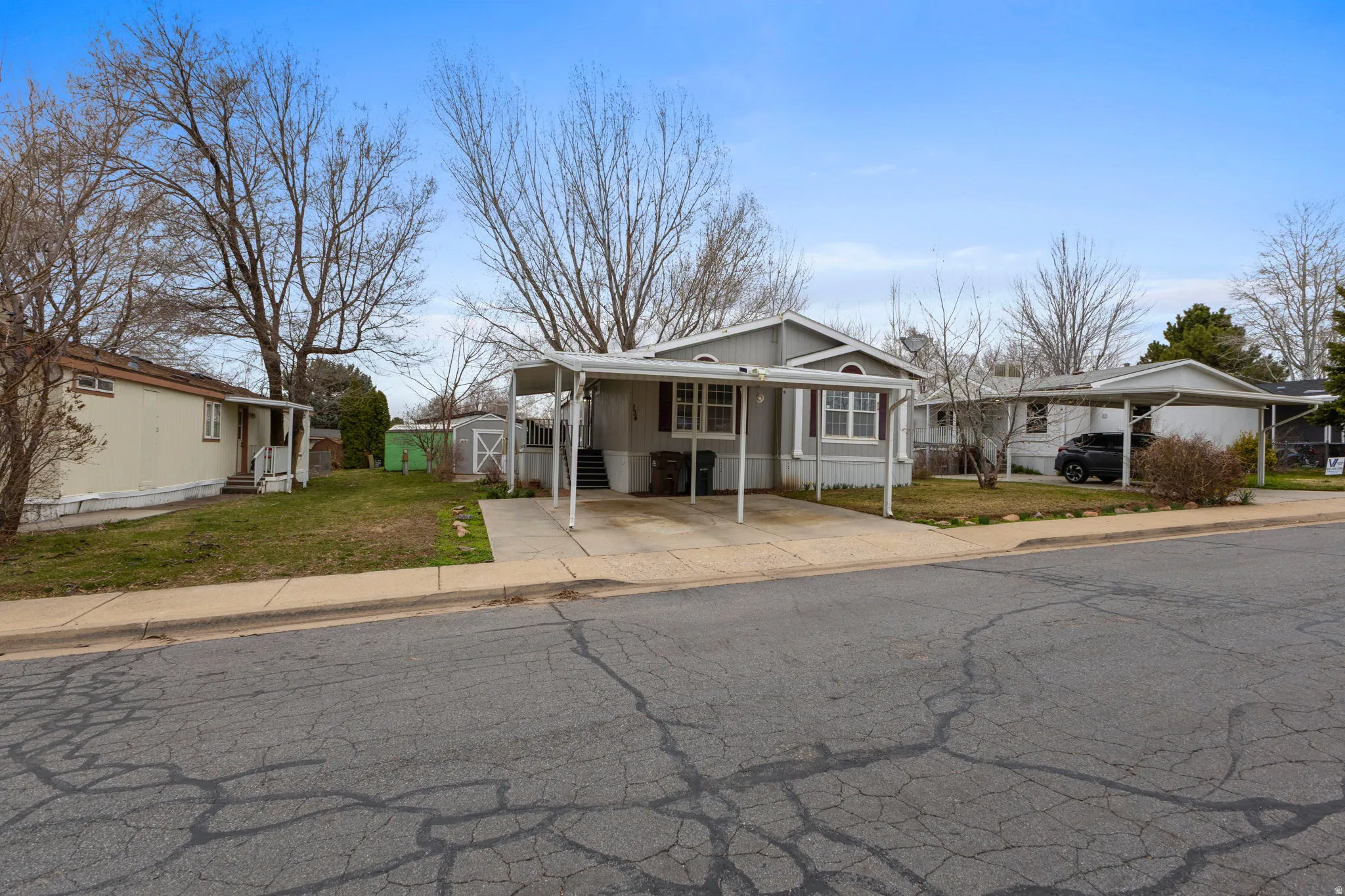 View of front of property with a front yard, a storage shed, driveway, an attached carport, and a residential view