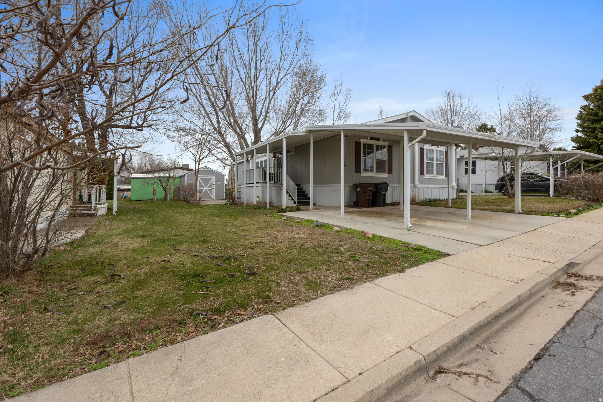 View of front of home with a front yard, a carport, a storage unit, and covered porch