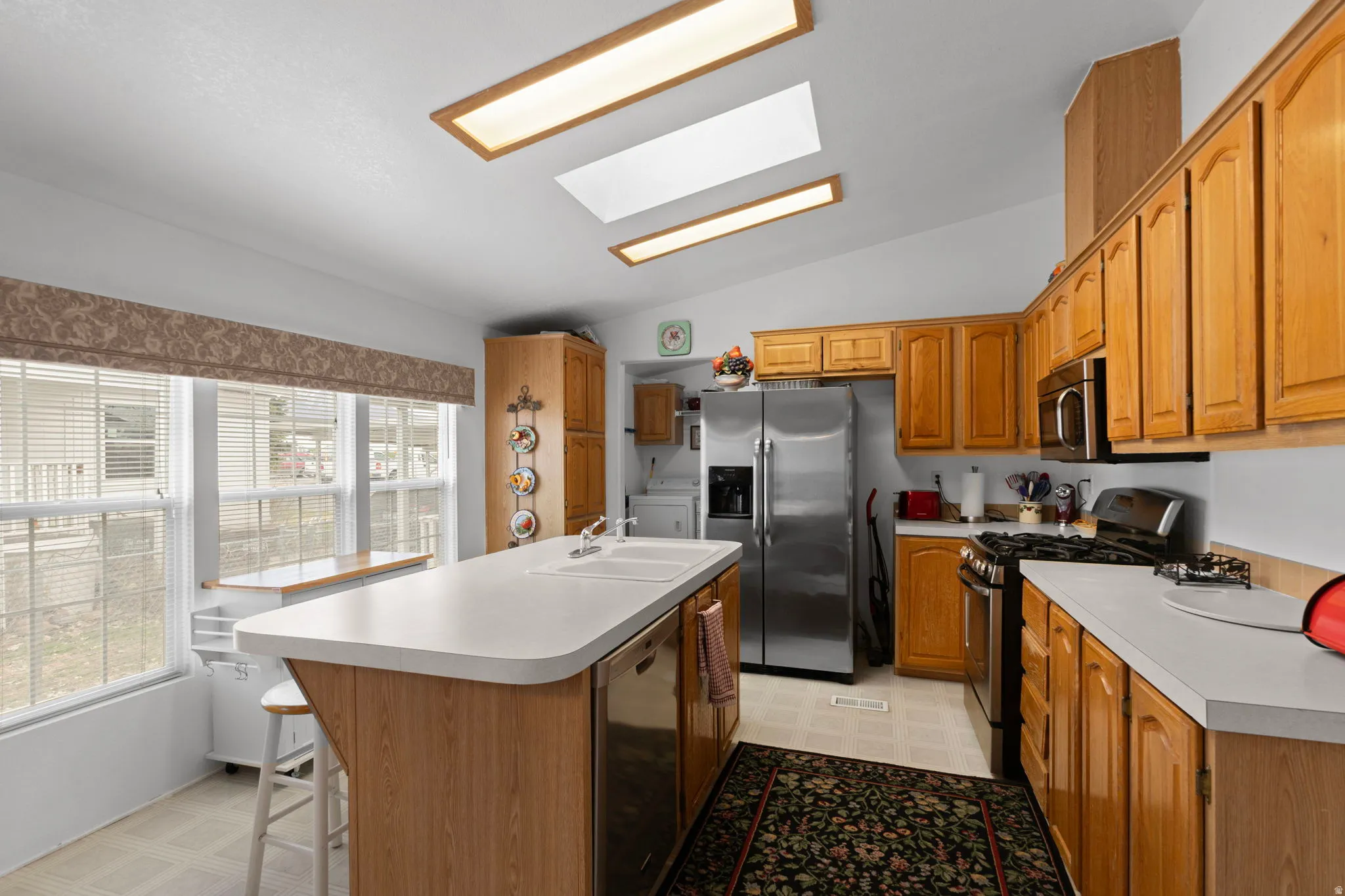 Kitchen featuring lofted ceiling, light flooring, stainless steel appliances, a skylight, and an island with sink