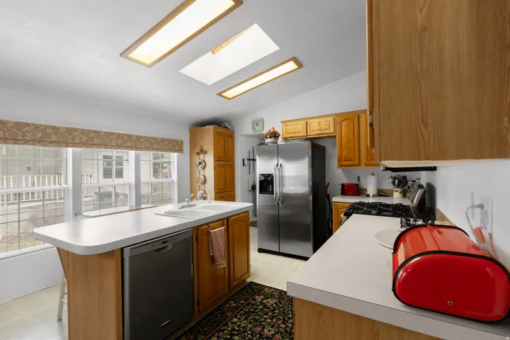Kitchen with a skylight, light flooring, stainless steel appliances, vaulted ceiling, and light countertops