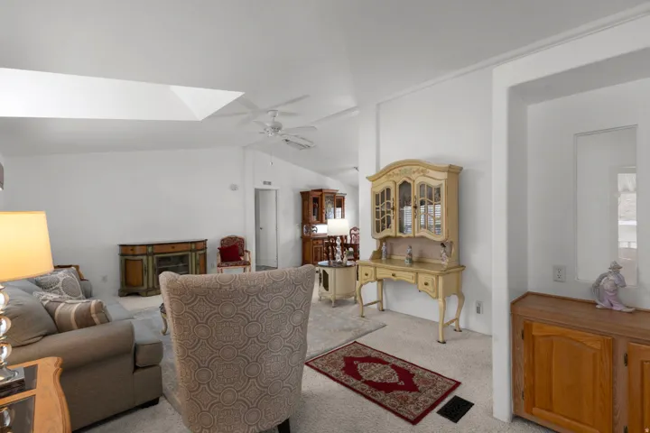 Living area featuring lofted ceiling, a ceiling fan, light colored carpet, and a fireplace