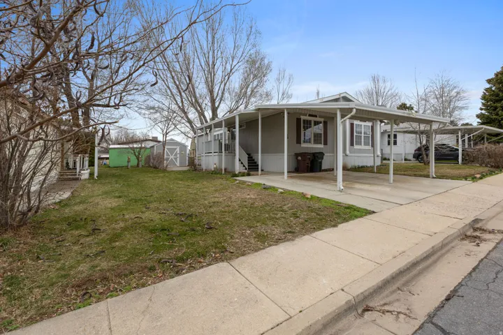 View of front of home with a front yard, a carport, a storage unit, and covered porch