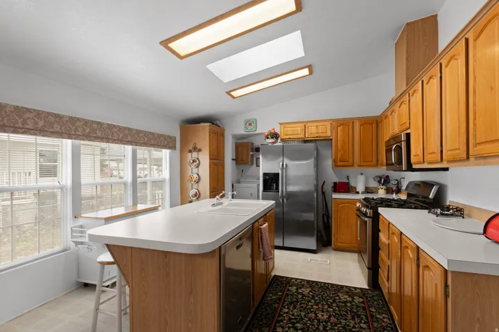 Kitchen featuring lofted ceiling, light flooring, stainless steel appliances, a skylight, and an island with sink