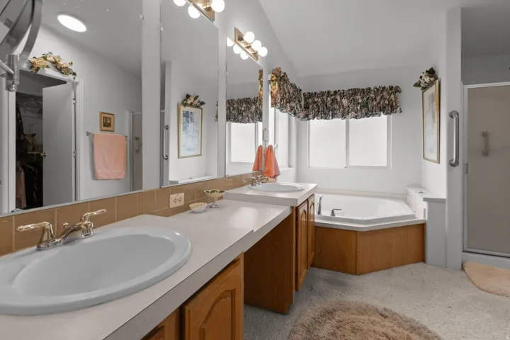 Bathroom with a stall shower, a garden tub, double vanity, and lofted ceiling