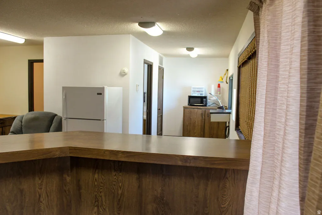 Kitchen with freestanding refrigerator, a textured ceiling, butcher block counters, and black microwave