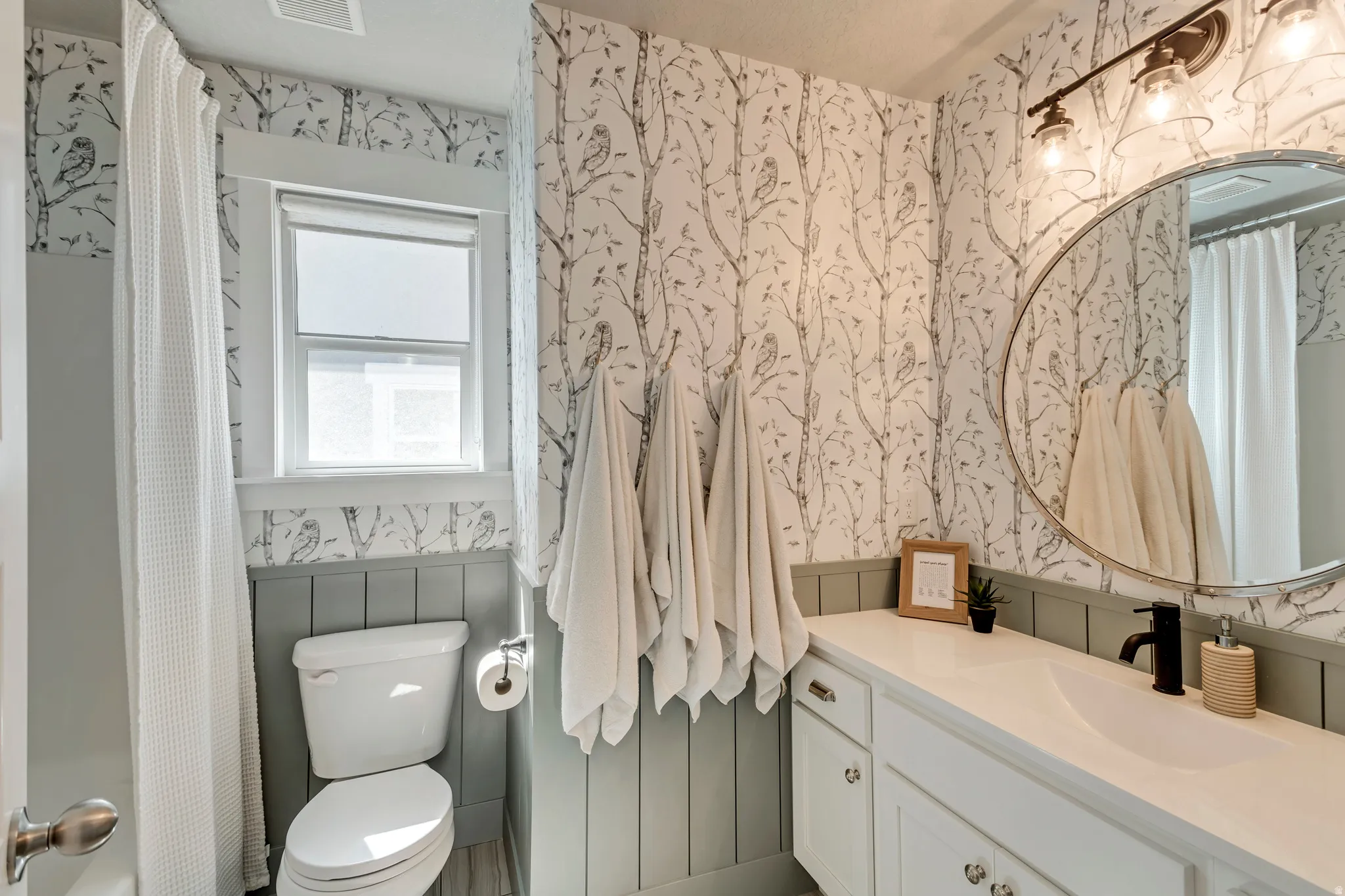 Full bath featuring wallpapered walls, vanity, and a wainscoted wall