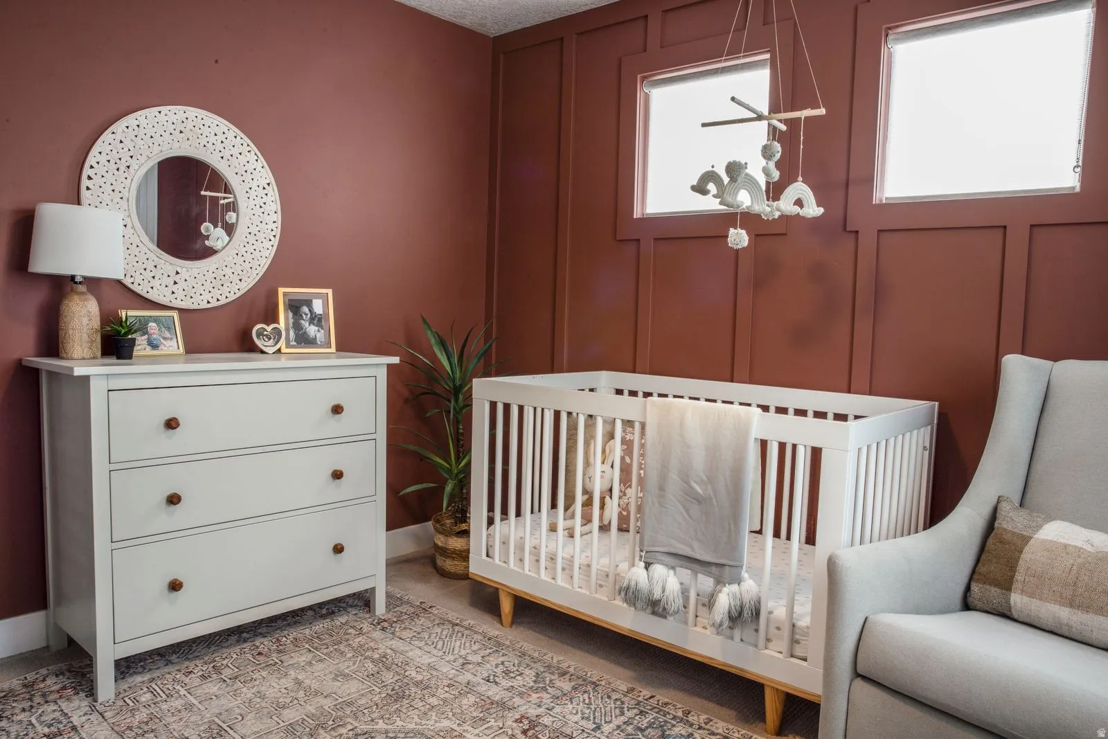 Bedroom with a decorative wall, multiple windows, a crib, and light carpet