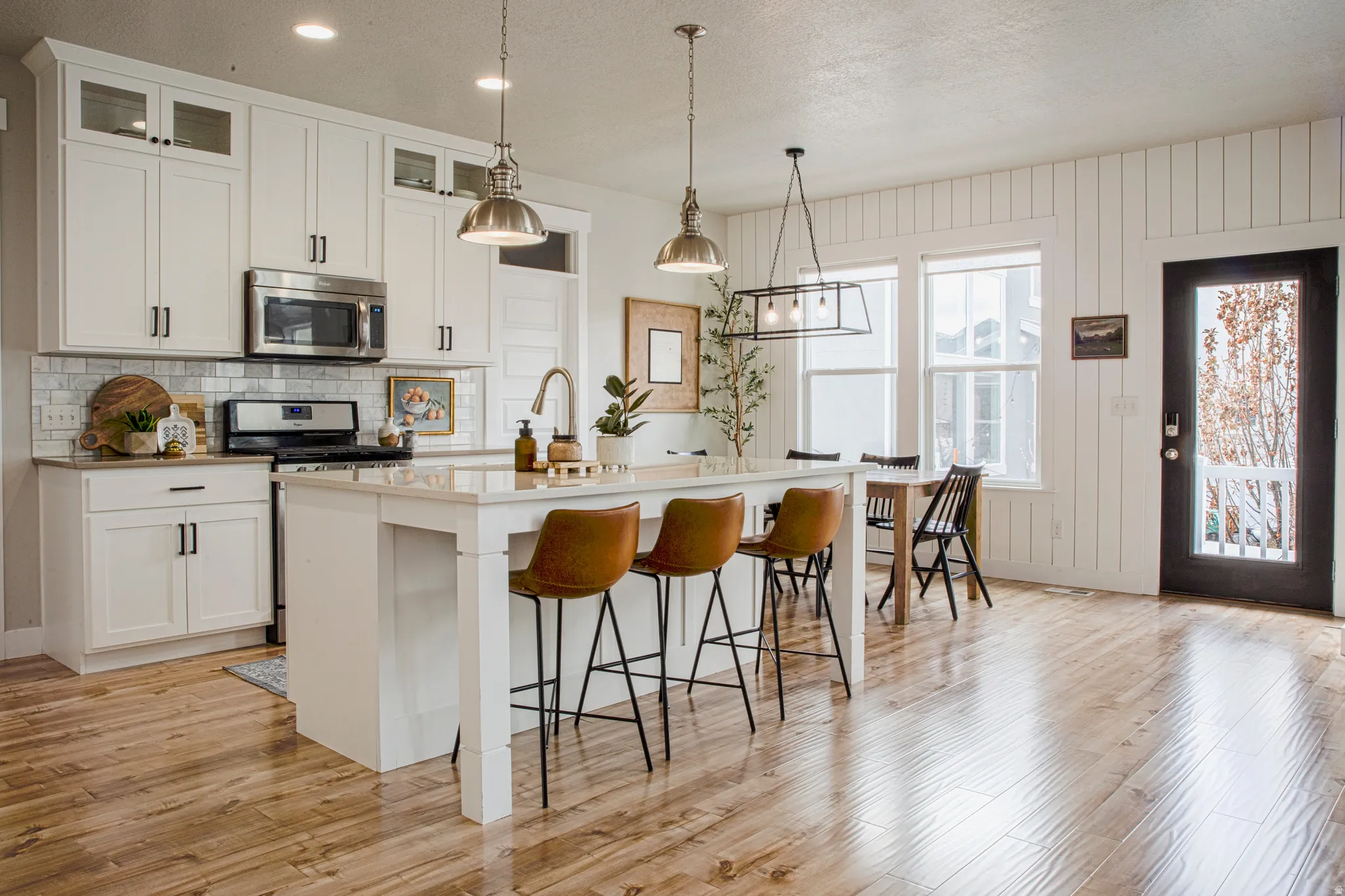 Kitchen with a breakfast bar area, an island with sink, white cabinets, light wood-type flooring, and a textured ceiling