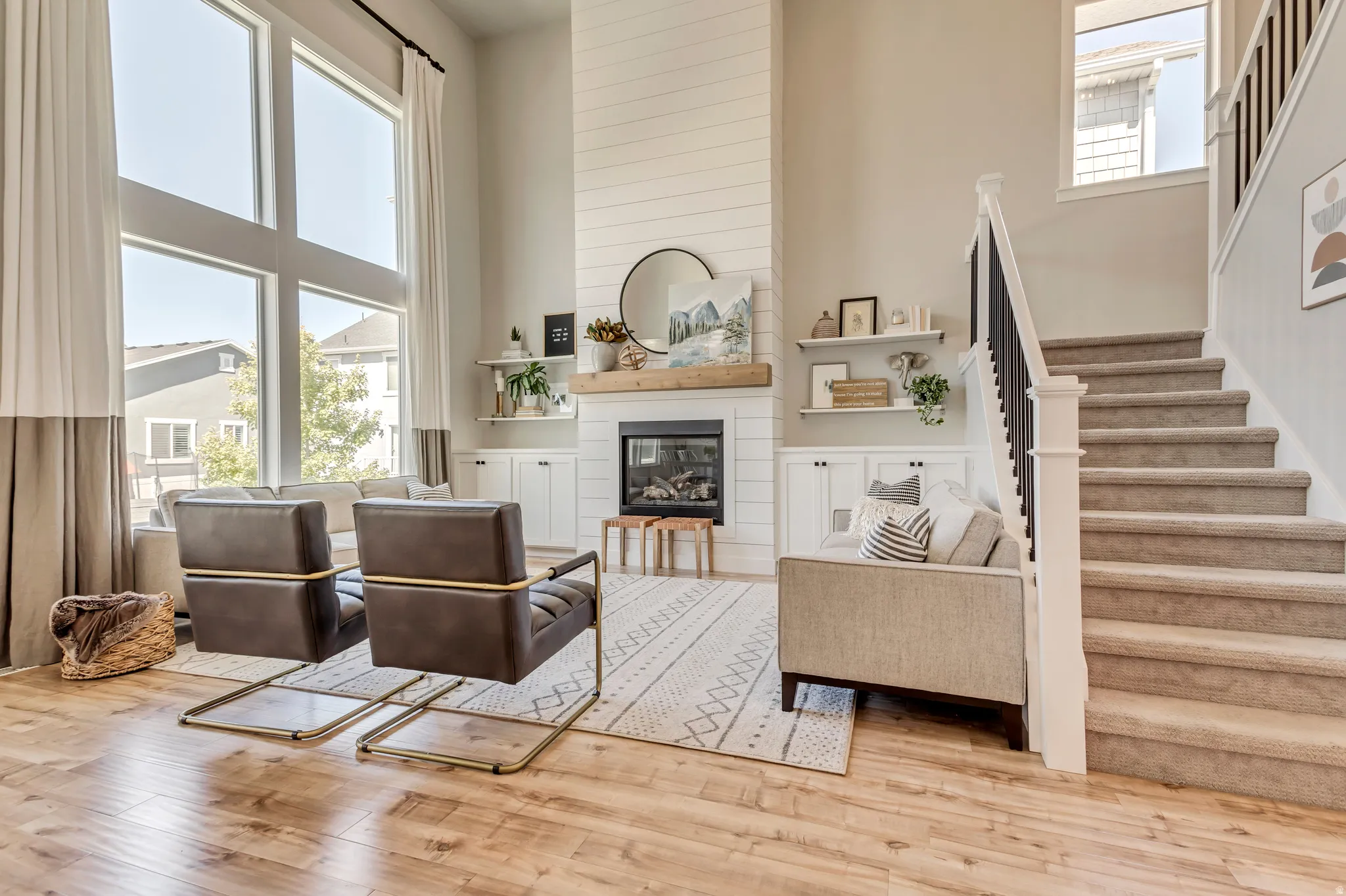 Living room with a high ceiling, healthy amount of natural light, a large fireplace, built-in cabinets, and wood finished floors