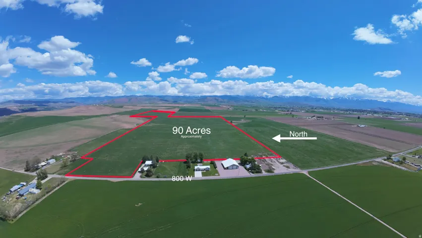 90-acre agricultural property with expansive green fields, established farm infrastructure including multiple outbuildings and equipment storage, mountain backdrop, and clear sightlines across productive acreage