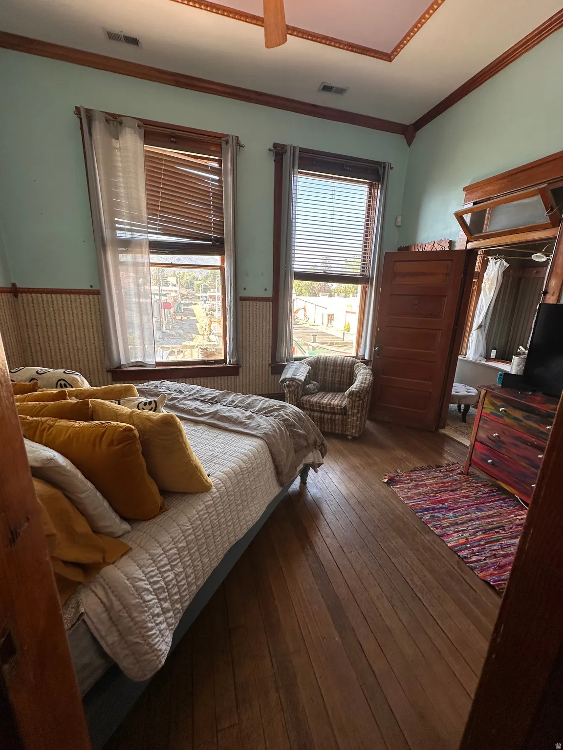 Bedroom featuring a wainscoted wall, ornamental molding, dark wood-style flooring, multiple windows, and ceiling fan