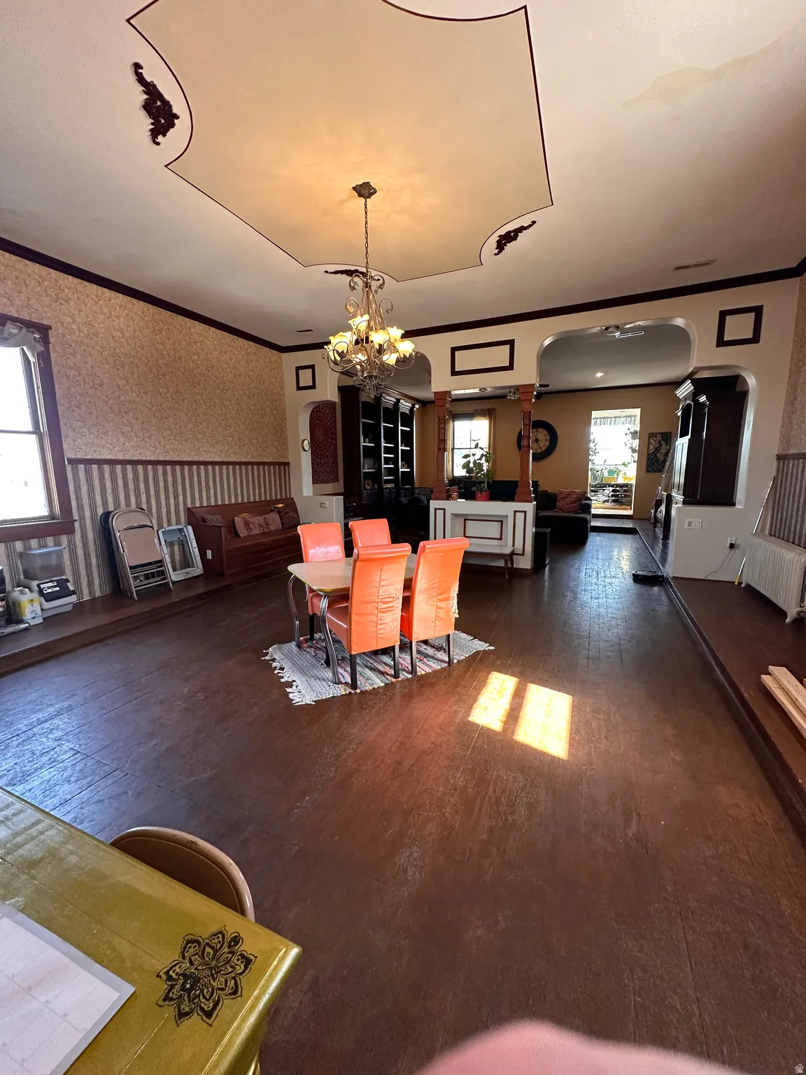 Dining space with wallpapered walls, ornamental molding, dark wood-style floors, arched walkways, and a chandelier