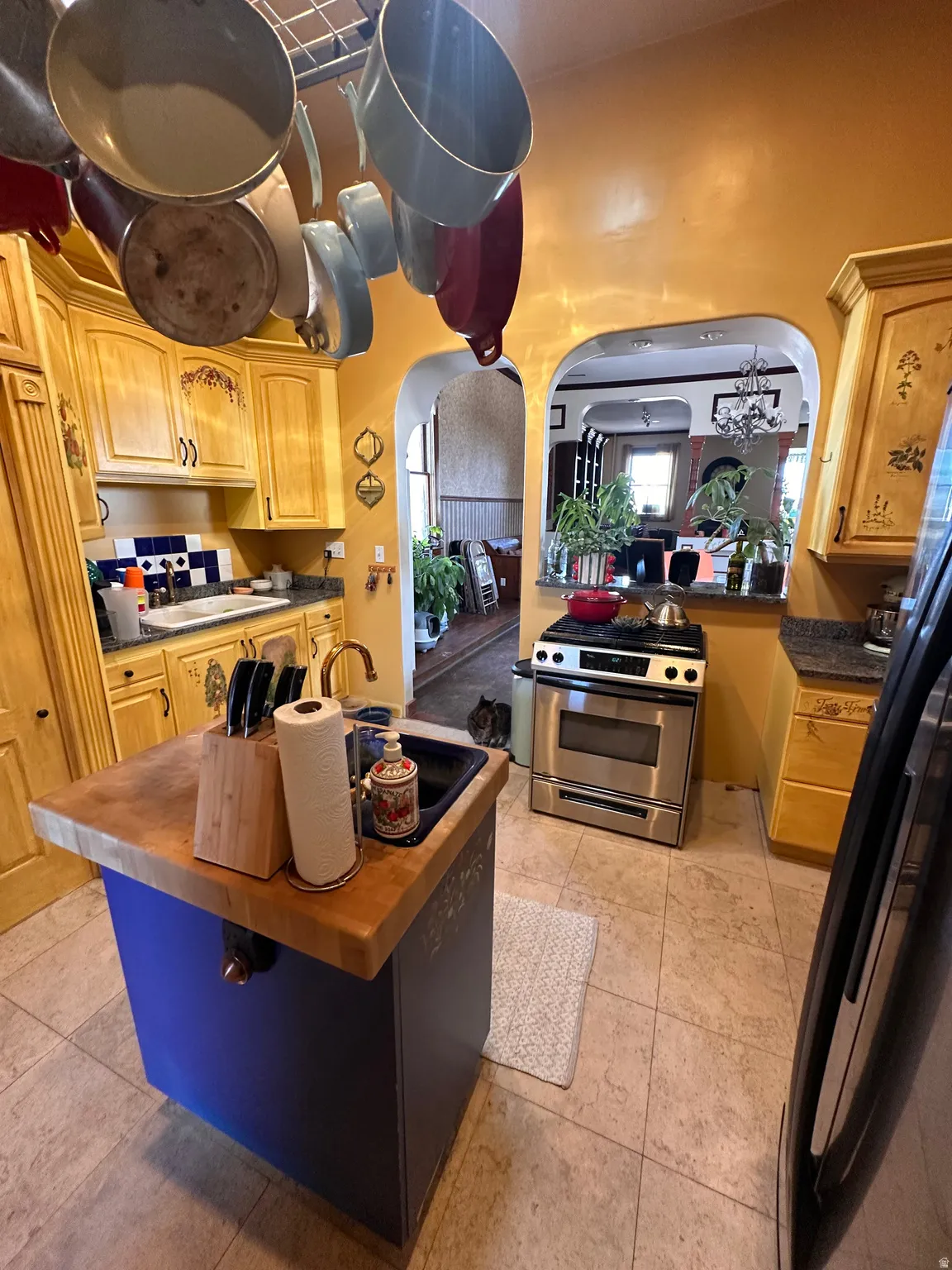 Kitchen with gas range, freestanding refrigerator, arched walkways, butcher block countertops, and a center island with sink