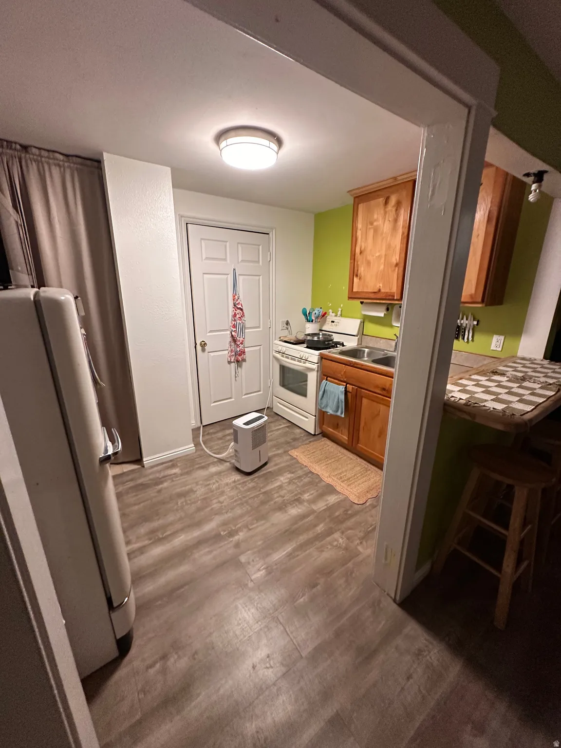 Kitchen featuring white gas range, wood finish cabinets, fridge, dark wood finished floors, and light countertops