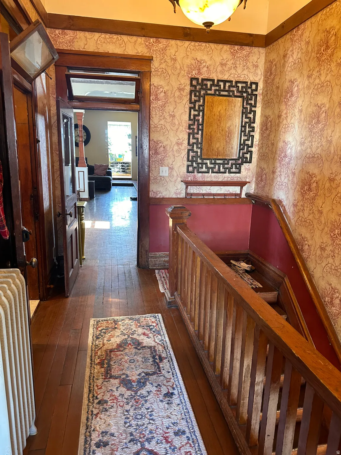 Hallway featuring dark wood-style flooring, radiator, and a wainscoted wall