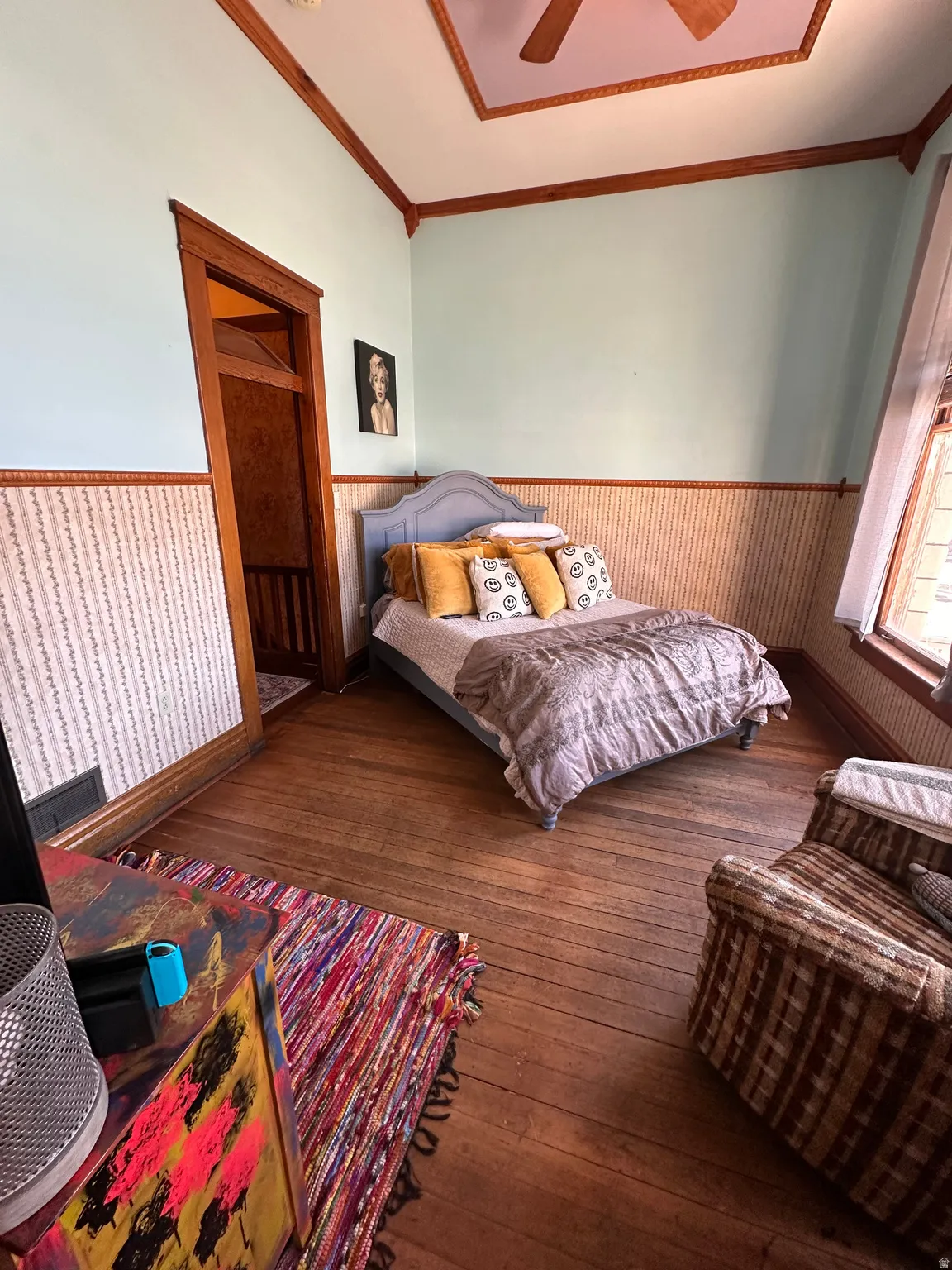 Bedroom with wainscoting, wood-type flooring, ornamental molding, and a ceiling fan