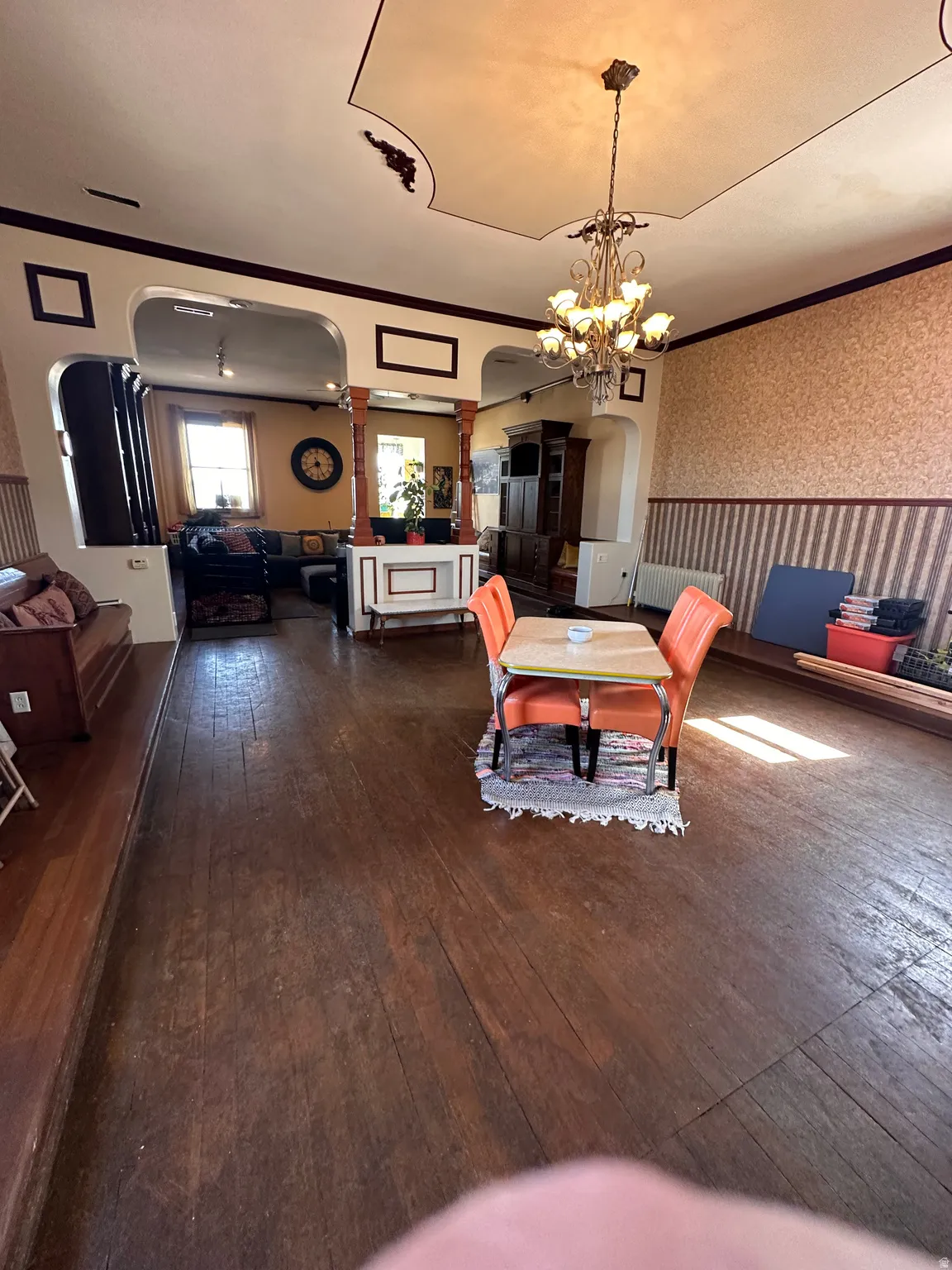 Dining area featuring wallpapered walls, arched walkways, ornamental molding, hanging lights, and dark wood finished floors