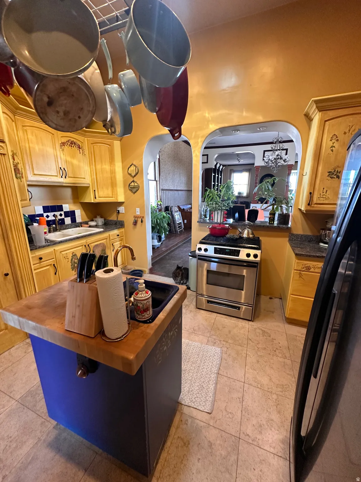 Kitchen with stainless steel gas range oven, freestanding refrigerator, arched walkways, butcher block countertops, and a kitchen island with sink