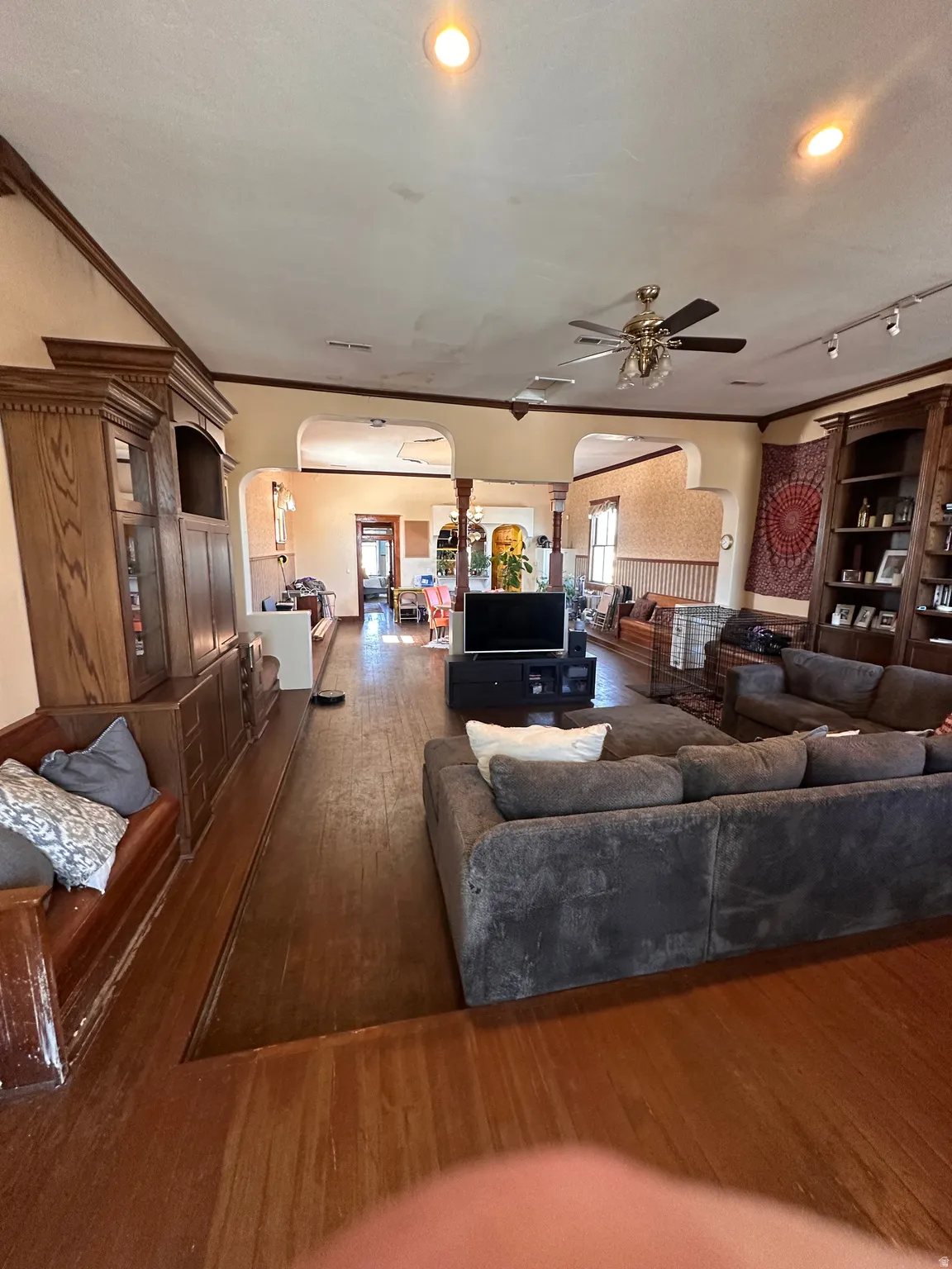 Living room with arched walkways, dark wood-style flooring, ornamental molding, and a ceiling fan