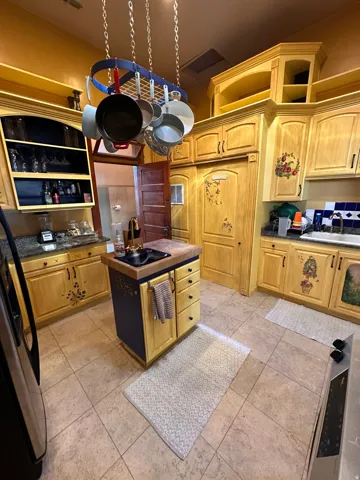 Kitchen with dark countertops, freestanding refrigerator, a kitchen island with sink, and light wood finish cabinetry