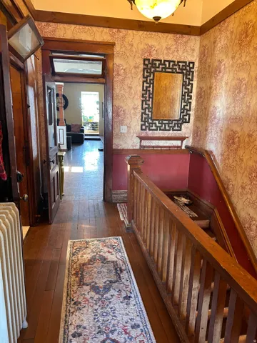Hallway featuring dark wood-style flooring, radiator, and a wainscoted wall