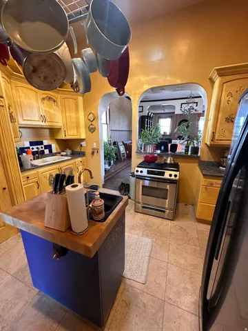 Kitchen with stainless steel gas range oven, freestanding refrigerator, arched walkways, butcher block countertops, and a kitchen island with sink