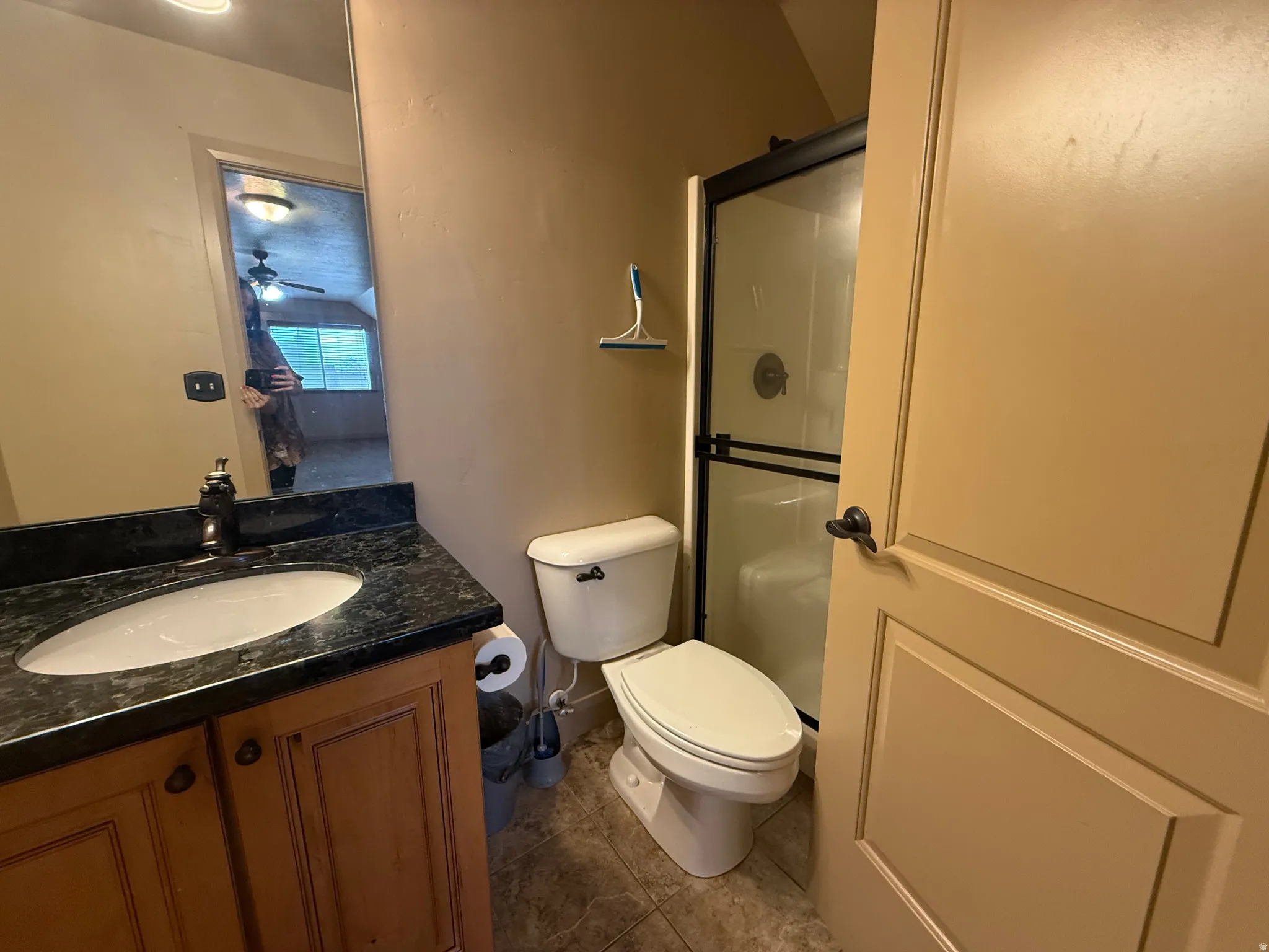 Bathroom featuring a shower stall, vanity, dark tile patterned flooring, and ceiling fan