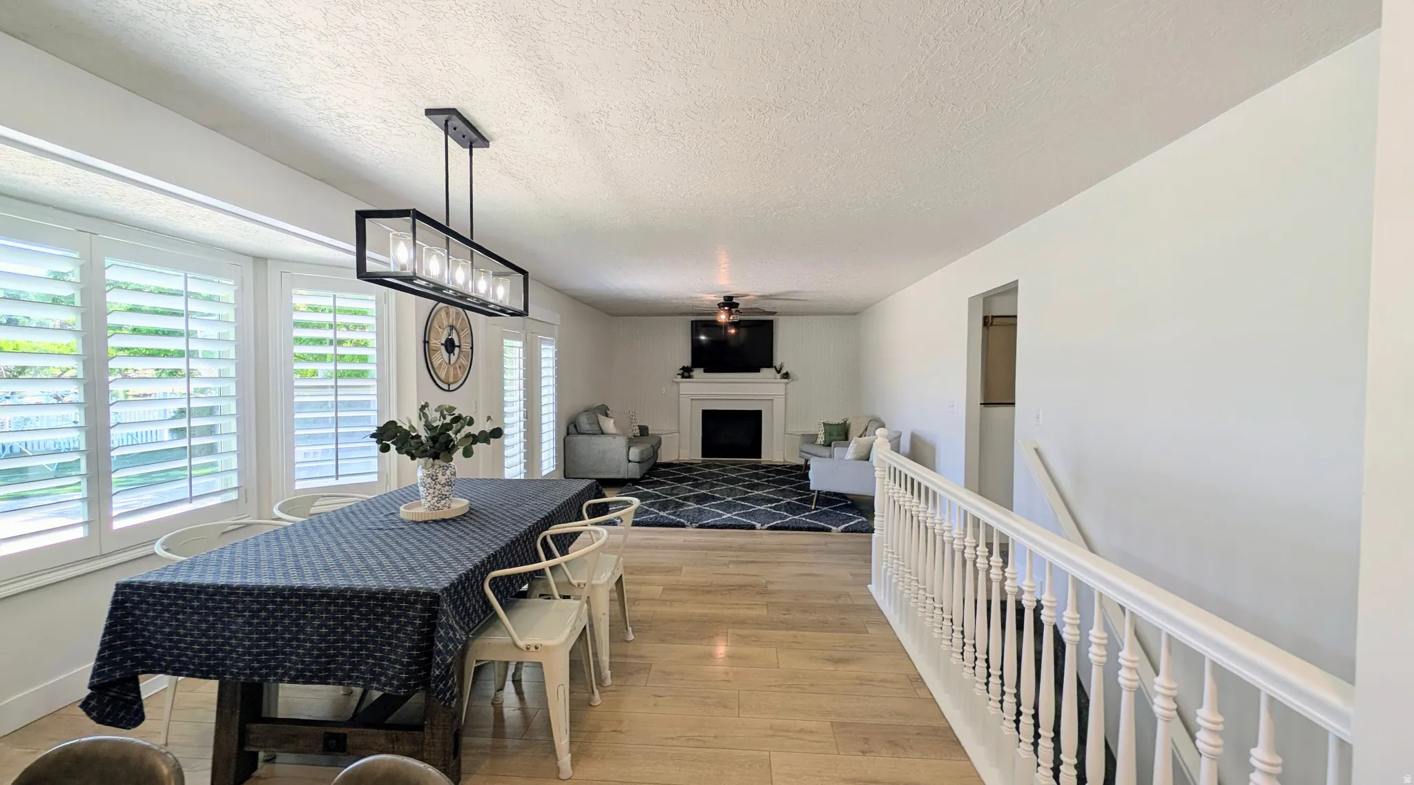 Spacious dining area featuring wood-finish flooring, a linear chandelier, and multiple windows with plantation shutters