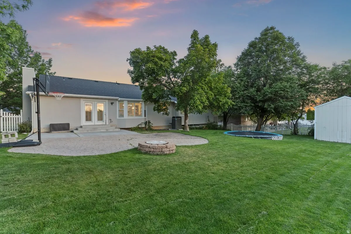 Expansive backyard featuring a manicured lawn, established trees, and a durable white picket fence