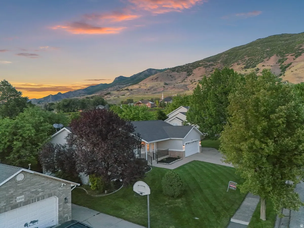Ranch-style residence featuring a two-car garage, mature landscaping, and a mountain backdrop
