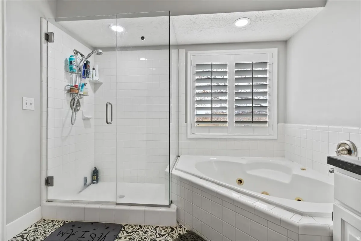 Full bath featuring a shower stall, a jetted tub, a textured ceiling, recessed lighting, and tile patterned flooring