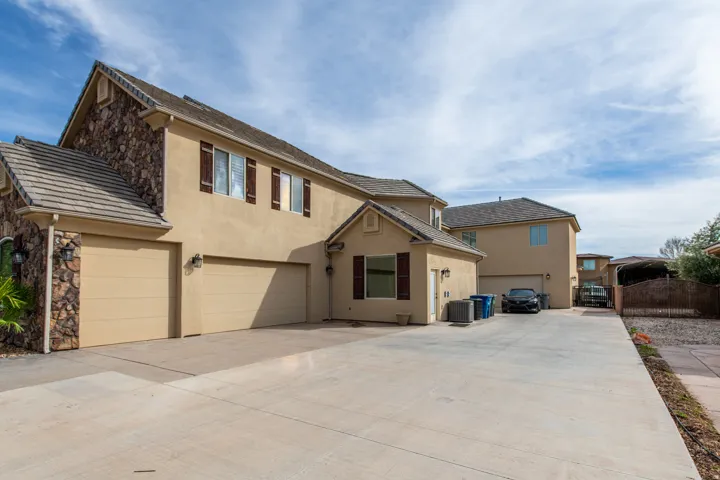 Traditional home with stucco siding, driveway, stone siding, and a gate