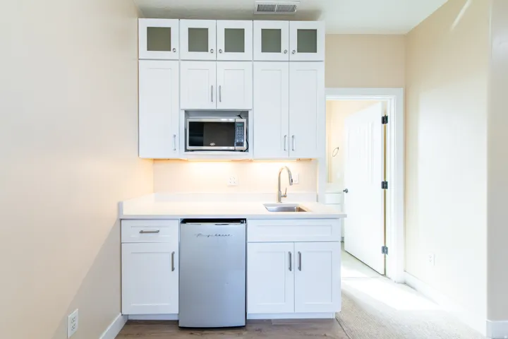 Kitchen featuring white cabinetry, white dishwasher, stainless steel microwave, glass fronted cabinets, and light stone counters