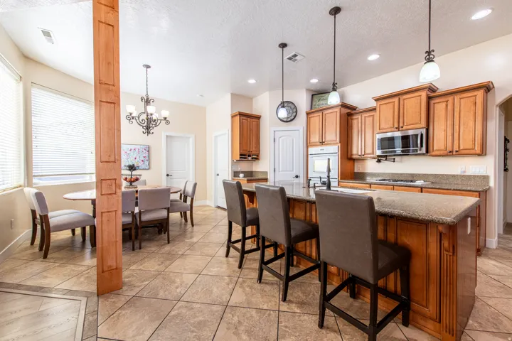 Kitchen with wood finish cabinets, suspended lighting, dark stone counters, stainless steel appliances, and an island with sink