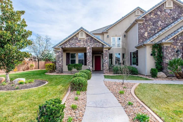 View of front of home featuring stucco siding, stone siding, and a balcony