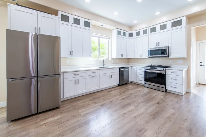 Kitchen featuring stainless steel appliances, glass insert cabinets, white cabinetry, light wood-style flooring, and recessed lighting