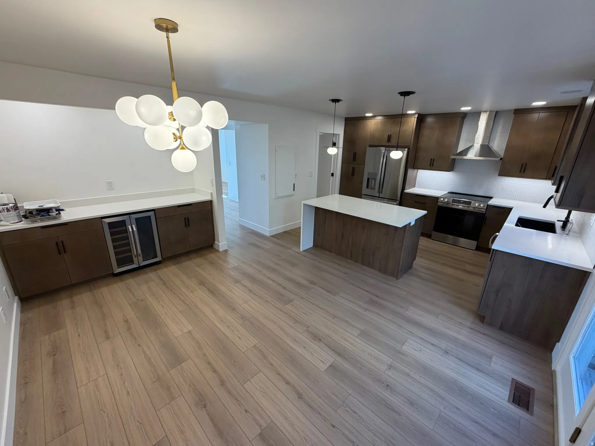 Kitchen featuring stainless steel appliances, dark wood finish cabinets, beverage cooler, light wood-type flooring, and hanging light fixtures