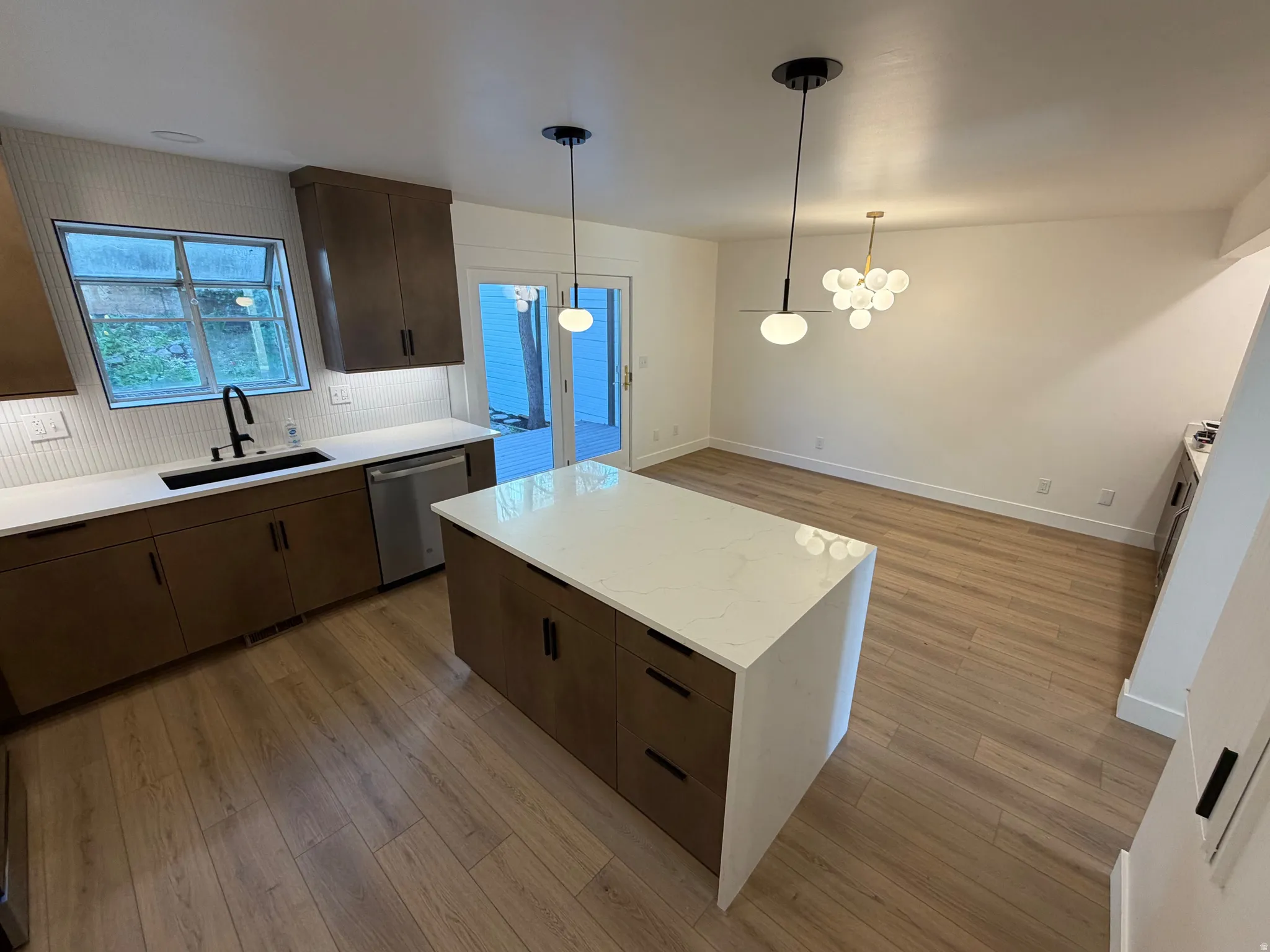 Kitchen with a kitchen island, light wood-type flooring, dark wood finish cabinetry, tasteful backsplash, and dishwasher