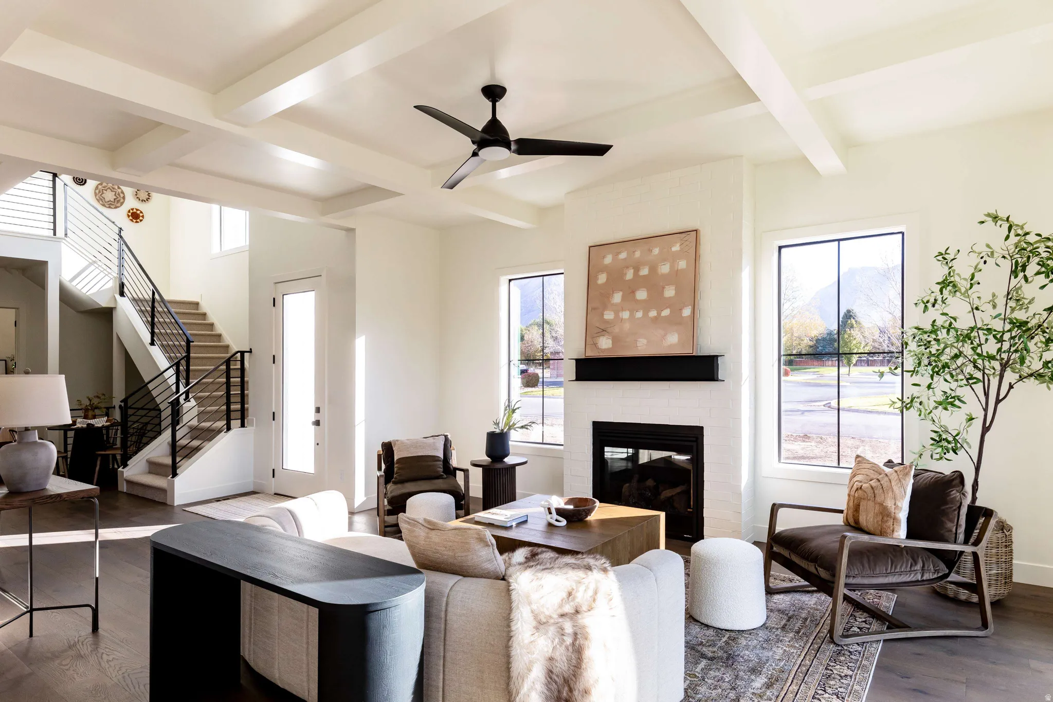 Living room with wood finished floors, a ceiling fan, coffered ceiling, a brick fireplace, and healthy amount of natural light