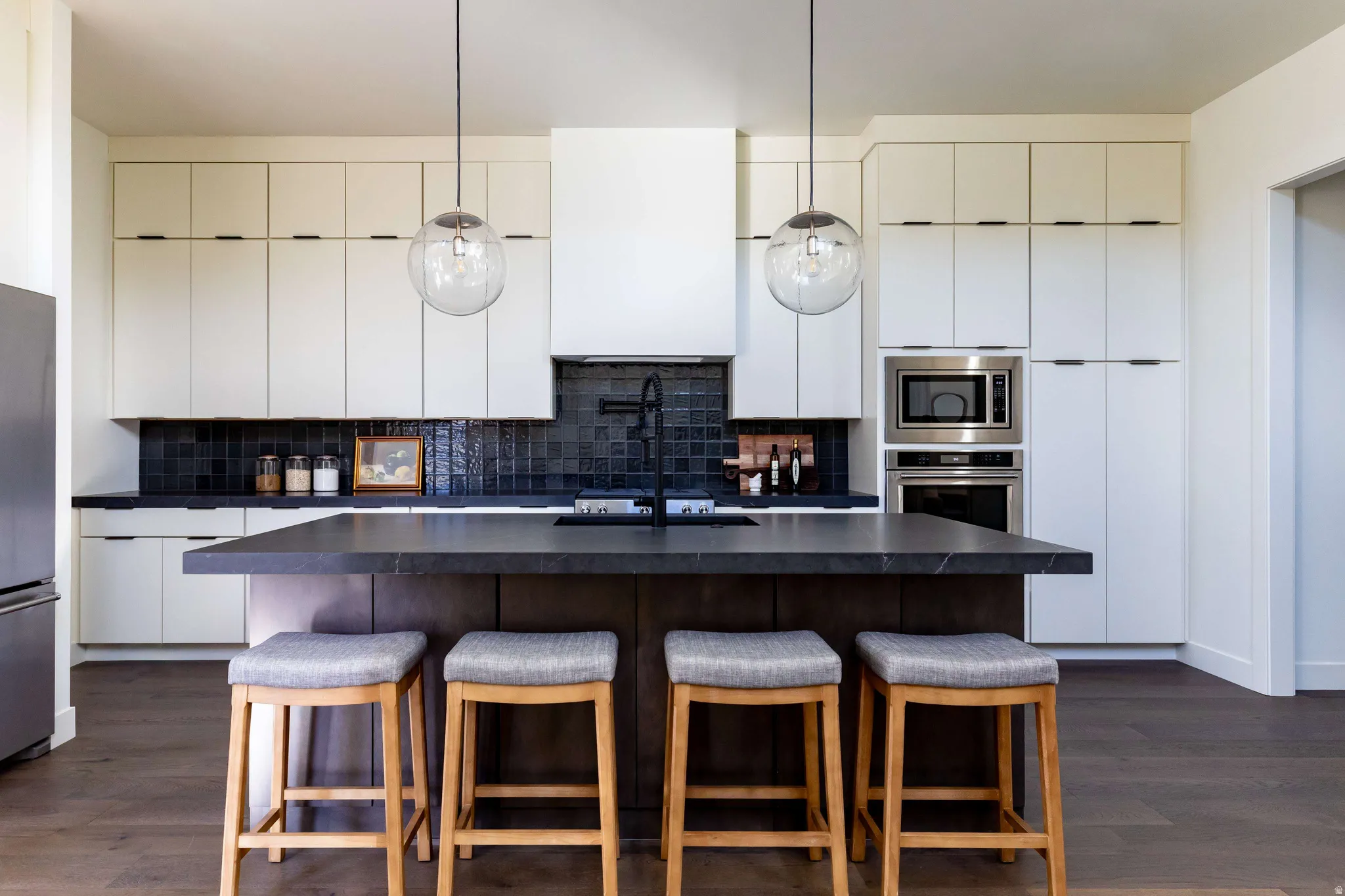 Kitchen featuring dark countertops, dark wood-type flooring, hanging light fixtures, and a breakfast bar