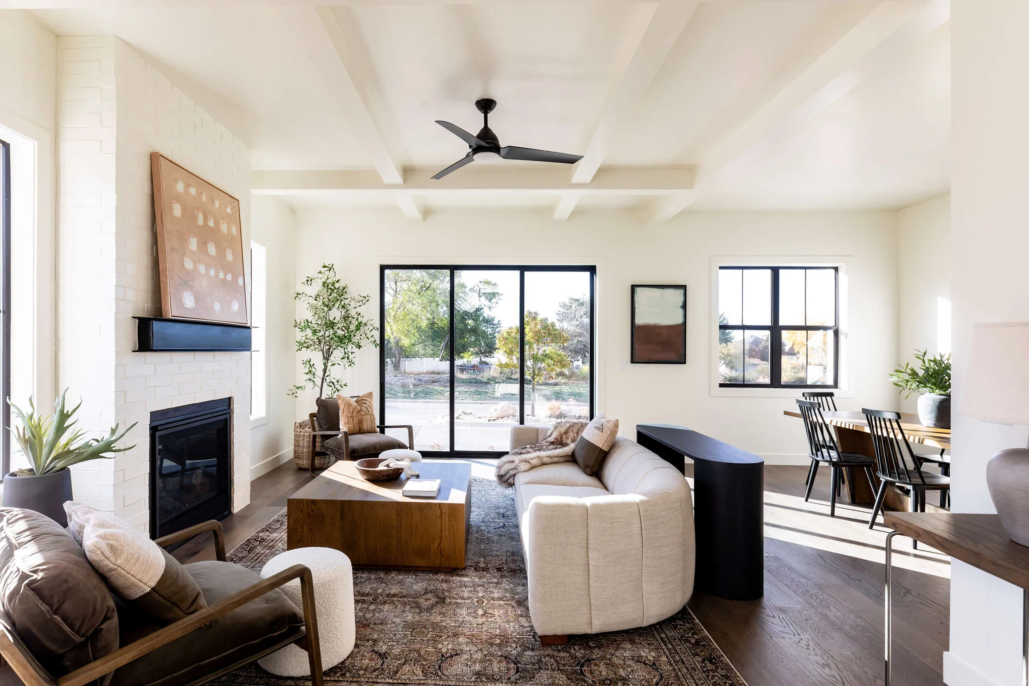 Living room featuring wood finished floors, ceiling fan, a brick fireplace, and beamed ceiling