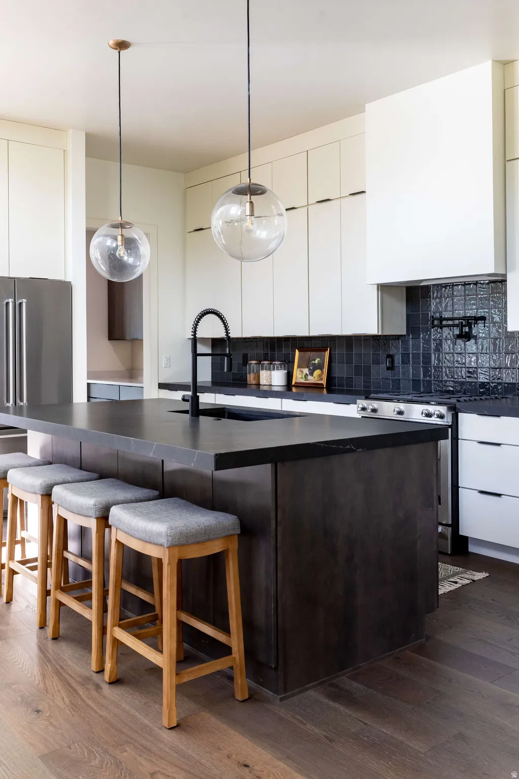 Kitchen with dark wood-type flooring, a kitchen bar, stainless steel gas stove, dual tone cabinetry, and decorative light fixtures