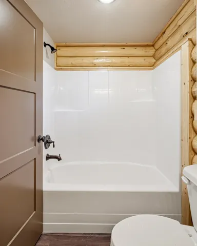 Full bath with dark wood finished floors and washtub / shower combination