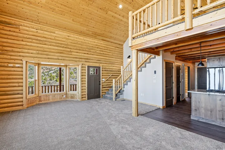 Unfurnished living room with dark carpet, a high ceiling, and rustic walls
