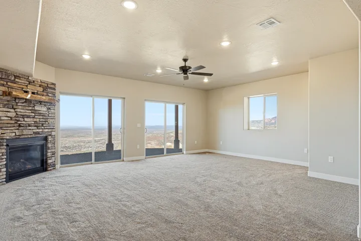 Unfurnished living room featuring a ceiling fan, a textured ceiling, carpet flooring, a stone fireplace, and recessed lighting