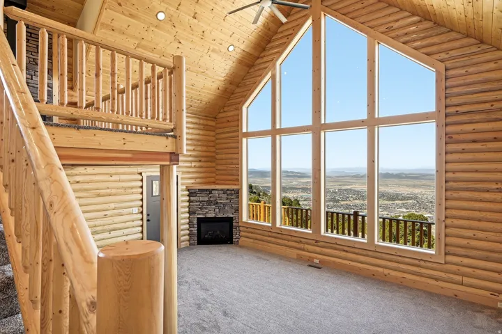Unfurnished living room with log walls, a high wood ceiling, carpet flooring, a stone fireplace, and ceiling fan