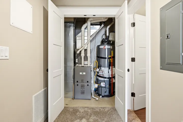 Utility room featuring electric panel, strapped water heater, and heating unit